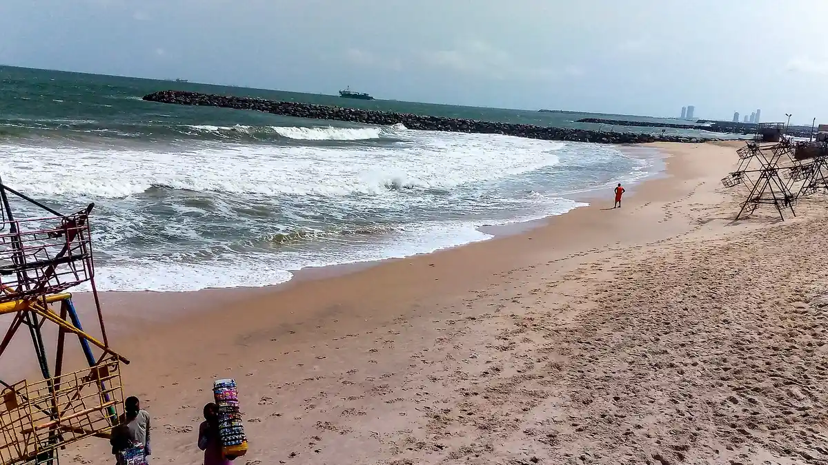 Waves breaking on the sand at Elegushi Beach, Lagos, with a rock breakwater, a ship offshore and metal beach swings
